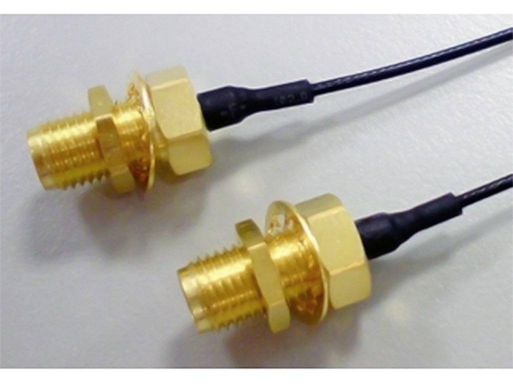 Zwei goldene Anschlussstecker mit schwarzen Kabeln liegen auf einer hellen Oberfläche.