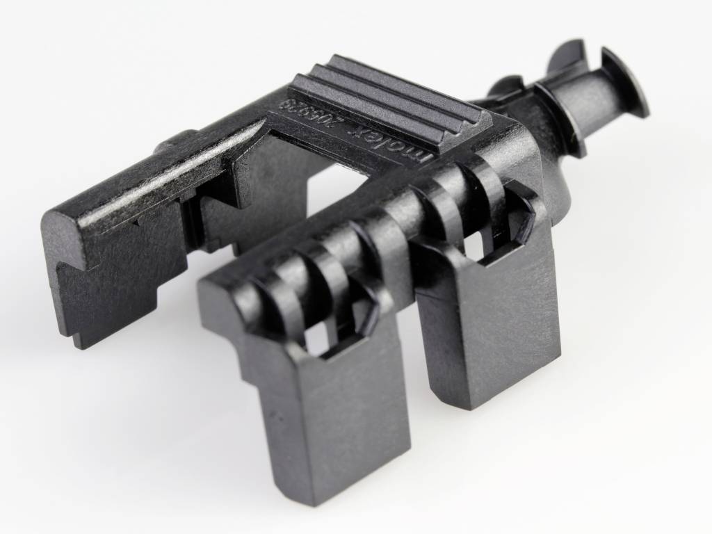 Plastikteil mit mehreren Öffnungen und eingraviertem Text, das möglicherweise Teil eines technischen oder Maschinenbausystems ist.