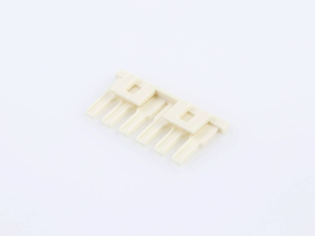 Ein kleiner, beiger Kunststoffstecker mit mehreren Pins liegt auf einer weißen Oberfläche.