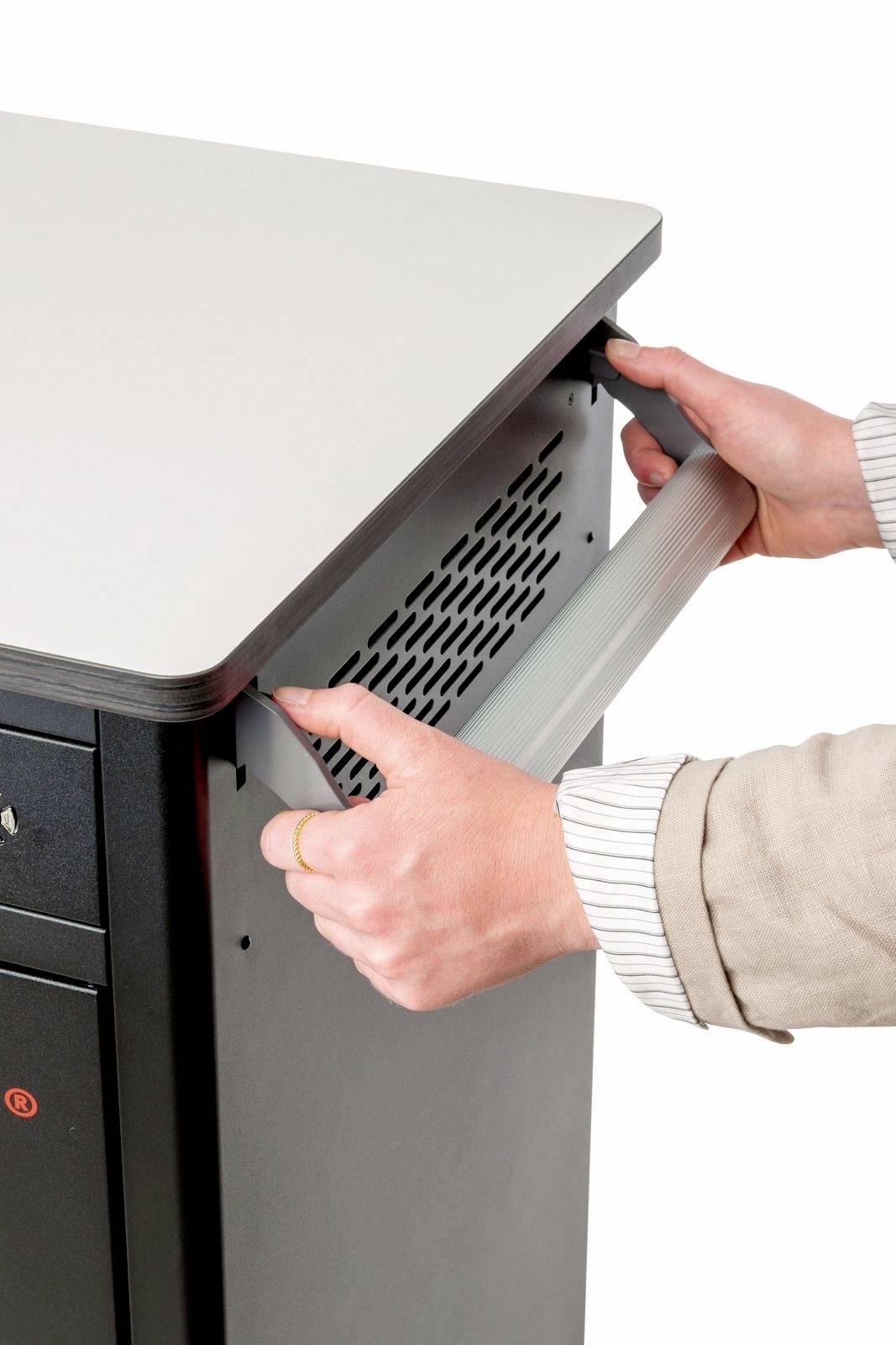 Person hält den Griff eines metallischen Möbelstücks mit Lüftungsschlitzen. Hände in Bewegung, als würde etwas geöffnet oder geschlossen.