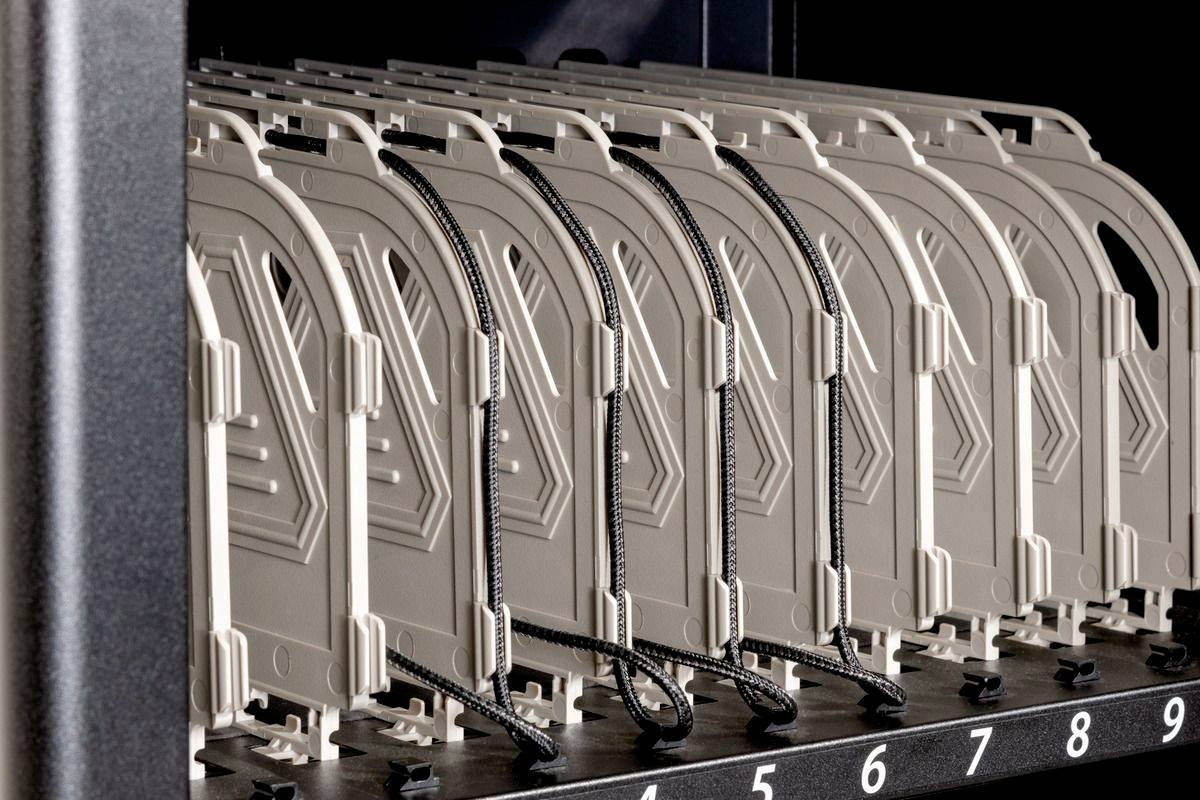 Eine Reihe von beige Servergehäusen in einem Rack, jeweils mit nummerierten Einschüben von 1 bis 9 und schwarzen Kabeln verbunden.