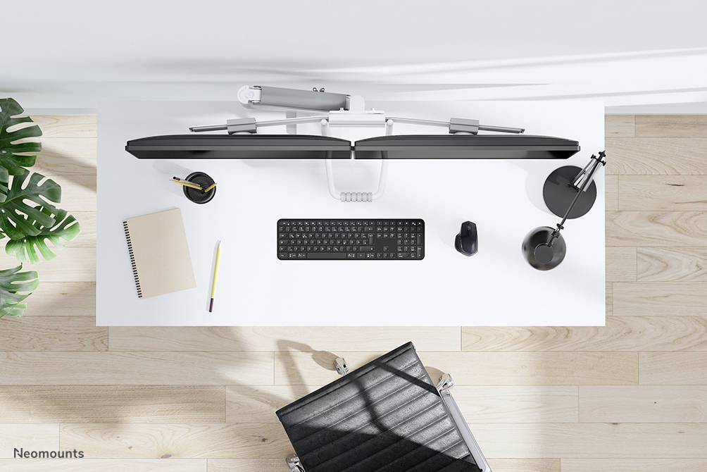 Schreibtisch von oben mit Tastatur, Monitorhalterung, Notizbuch, Stift, Maus und Lampe. Moderne Büroumgebung.