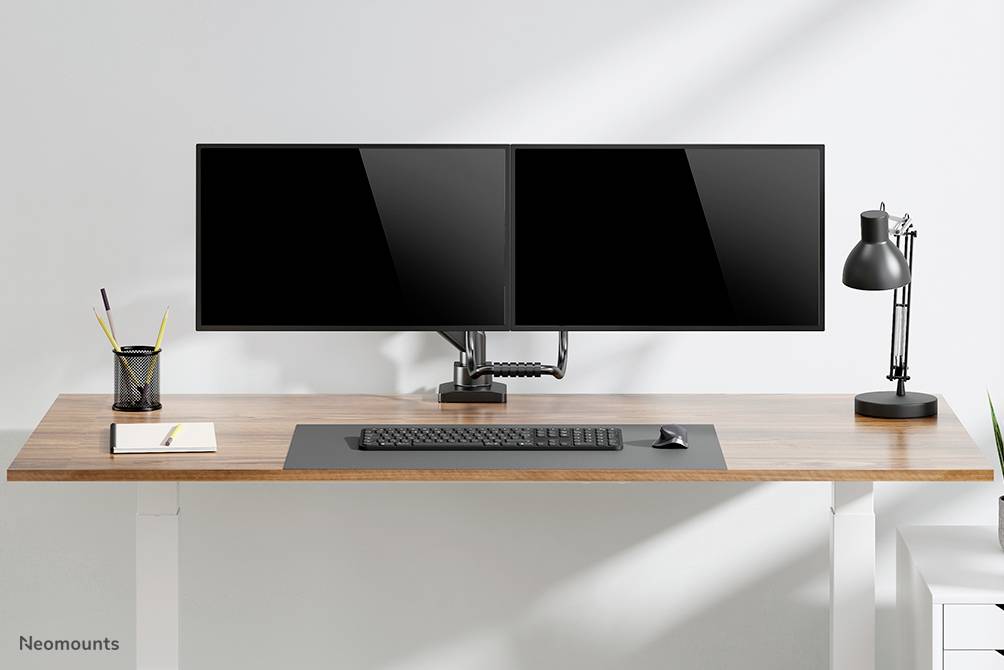 Ein aufgeräumter Schreibtisch mit zwei Monitoren, Tastatur, Schreibutensilien und einer Lampe. Minimalistisches, modernes Design.