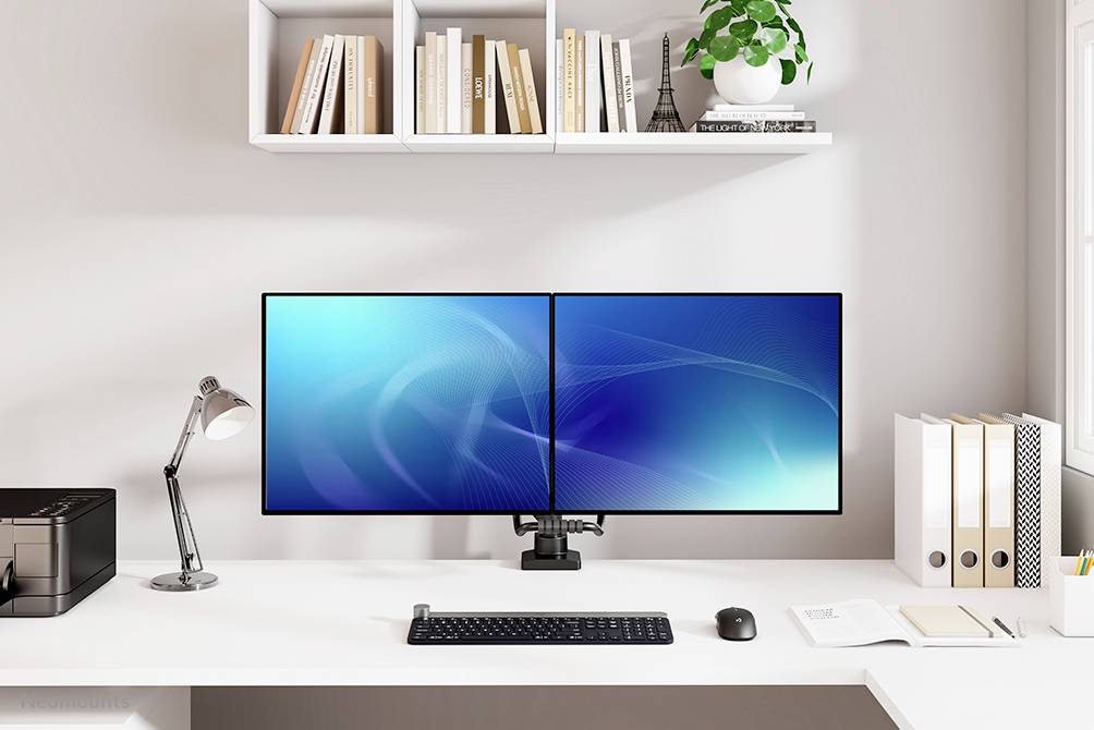 Ein sauberer, moderner Schreibtisch mit zwei nebeneinander stehenden Monitoren, einer Tastatur und Maus, Drucker, Lampe und Bücherregal.