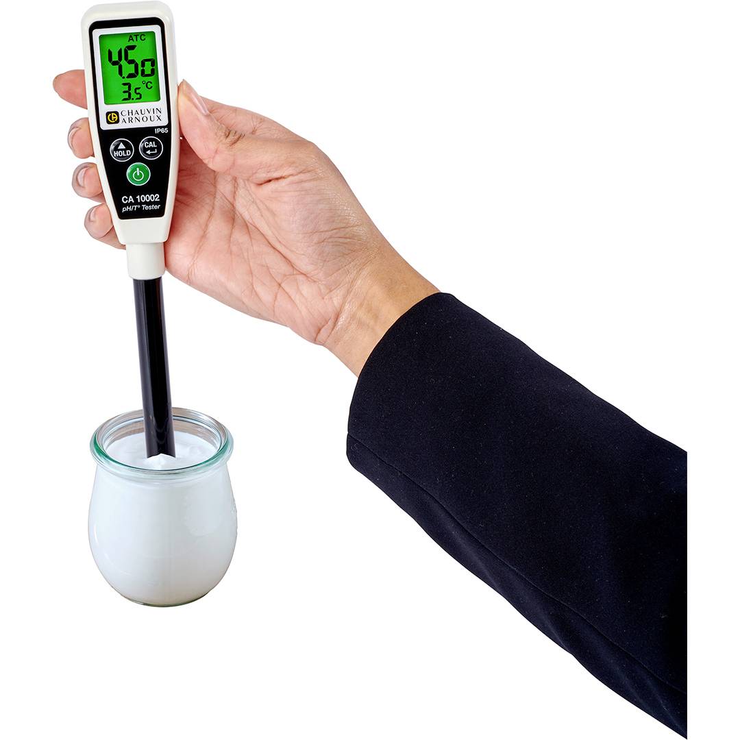 Hand hält ein digitales Thermometer, das in ein Glas mit weißer Flüssigkeit getaucht ist. Display zeigt 43,6°C an.