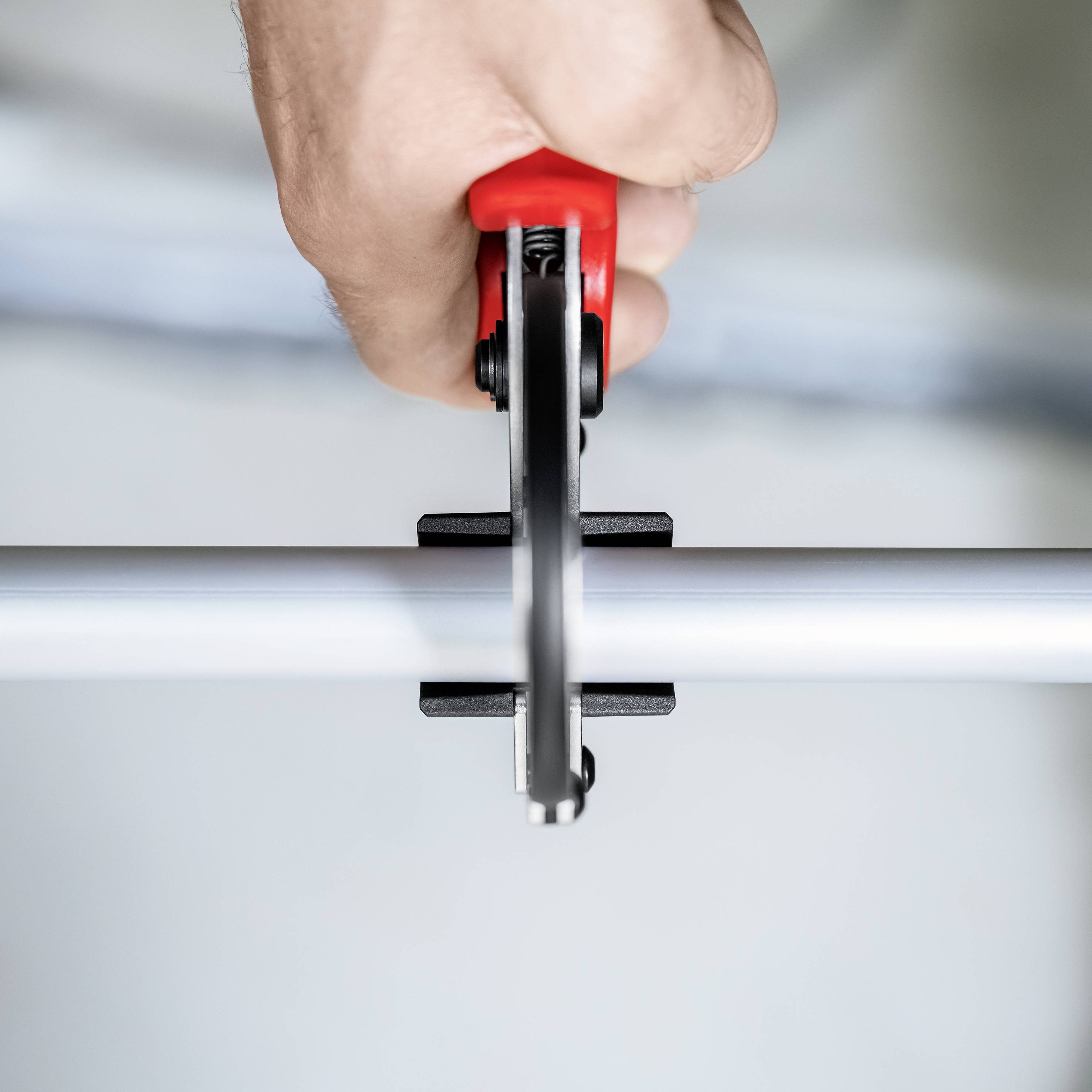 Eine Hand hält eine rote Handsäge und schneidet ein Metallrohr in Nahaufnahme.