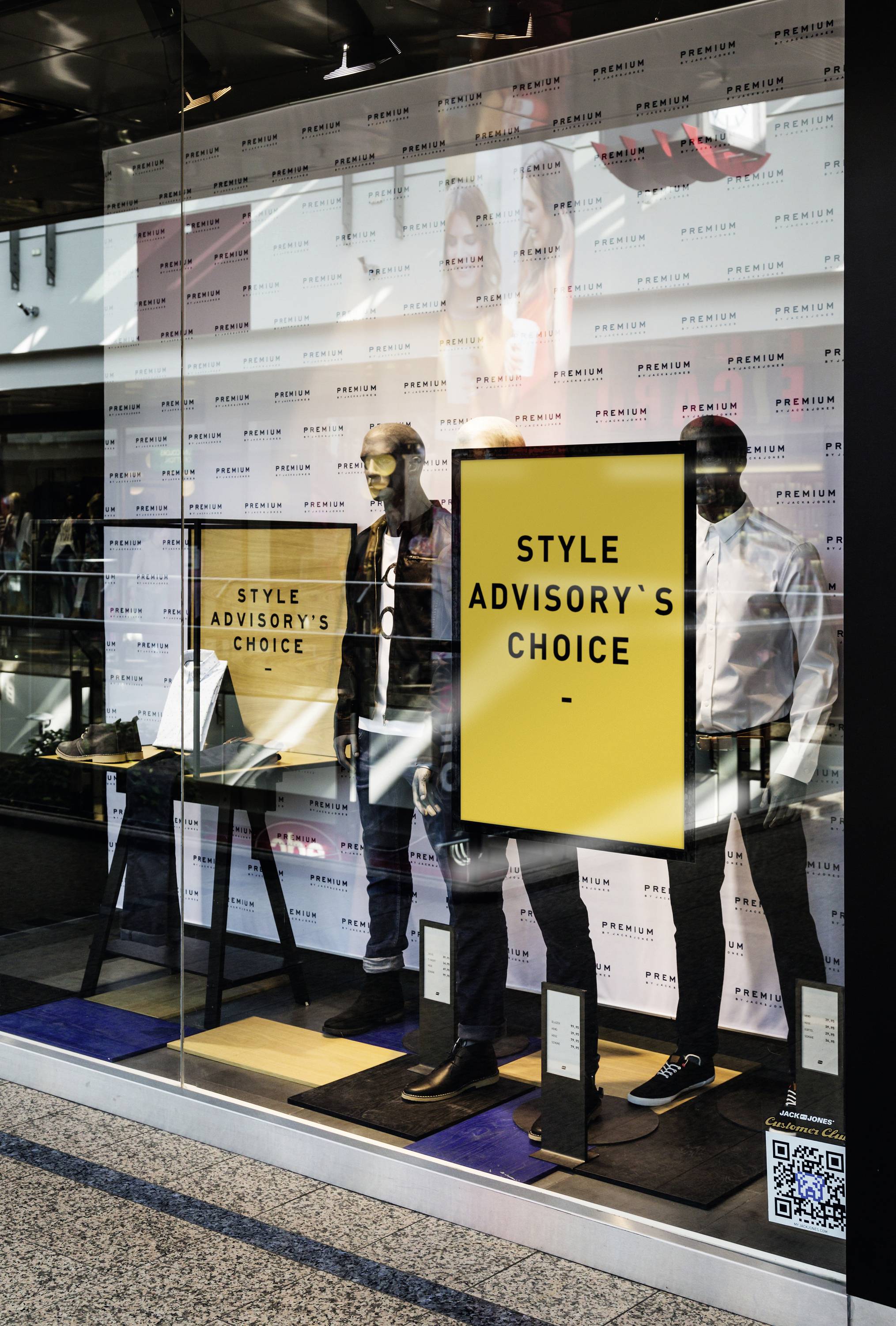 Ein Schaufenster mit zwei männlichen Schaufensterpuppen, die stilvolle Kleidung tragen. Ein gelbes Schild mit 'Style Advisory's Choice'.