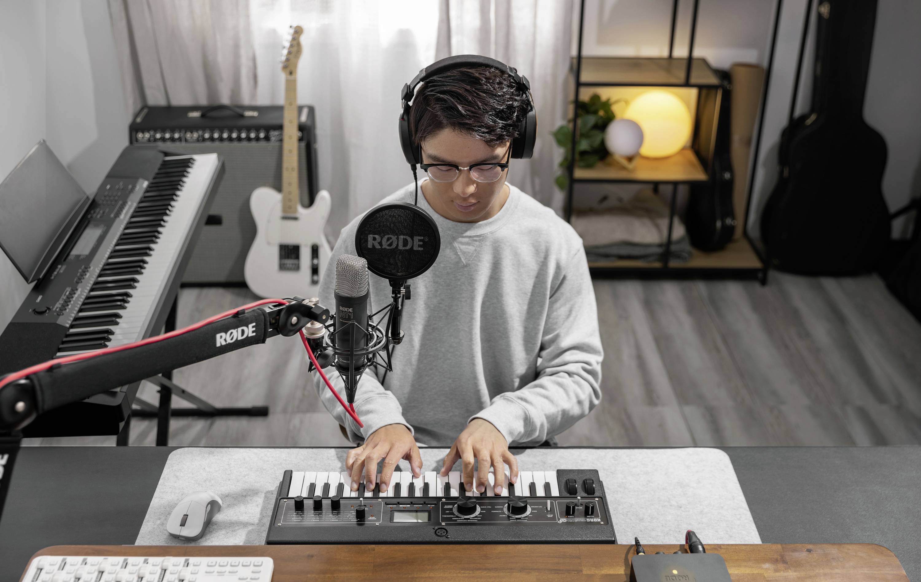 Eine Person spielt auf einem kleinen elektronischen Keyboard, trägt Kopfhörer und sitzt vor einem Mikrofon in einem Musikstudio.