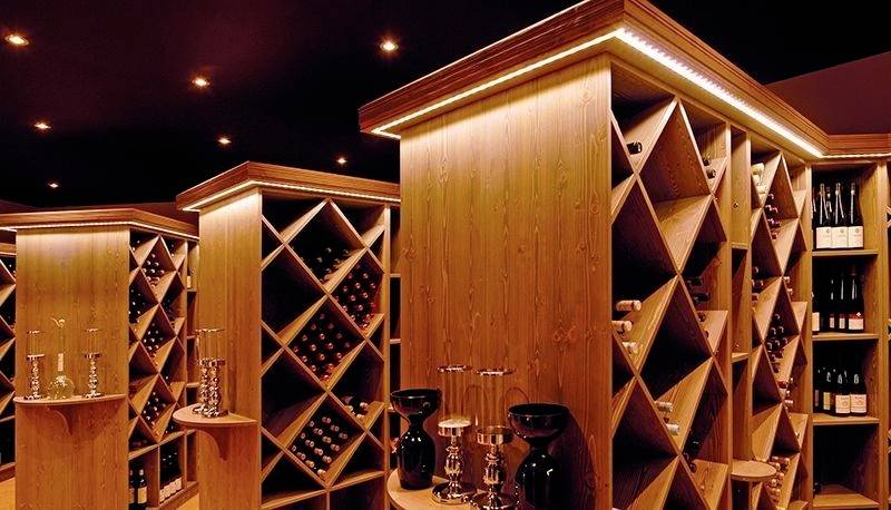 Ein stilvoller, moderner Weinkeller mit Holzregalen, die Weinflaschen und Gläser halten. Sanfte Beleuchtung schafft eine warme Atmosphäre.