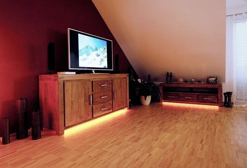 Ein Wohnzimmer mit Holzboden zeigt einen Fernseher auf einem Holzschrank, gedämpfte Beleuchtung sorgt für eine gemütliche Atmosphäre.