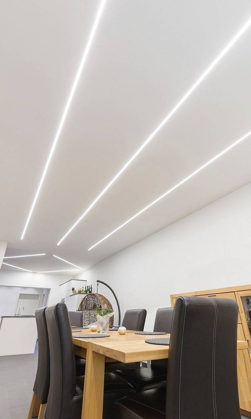 Esszimmer mit holzfarbenem Tisch und schwarzen Stühlen. Moderne Deckenbeleuchtung mit langen, schmalen LED-Streifen.
