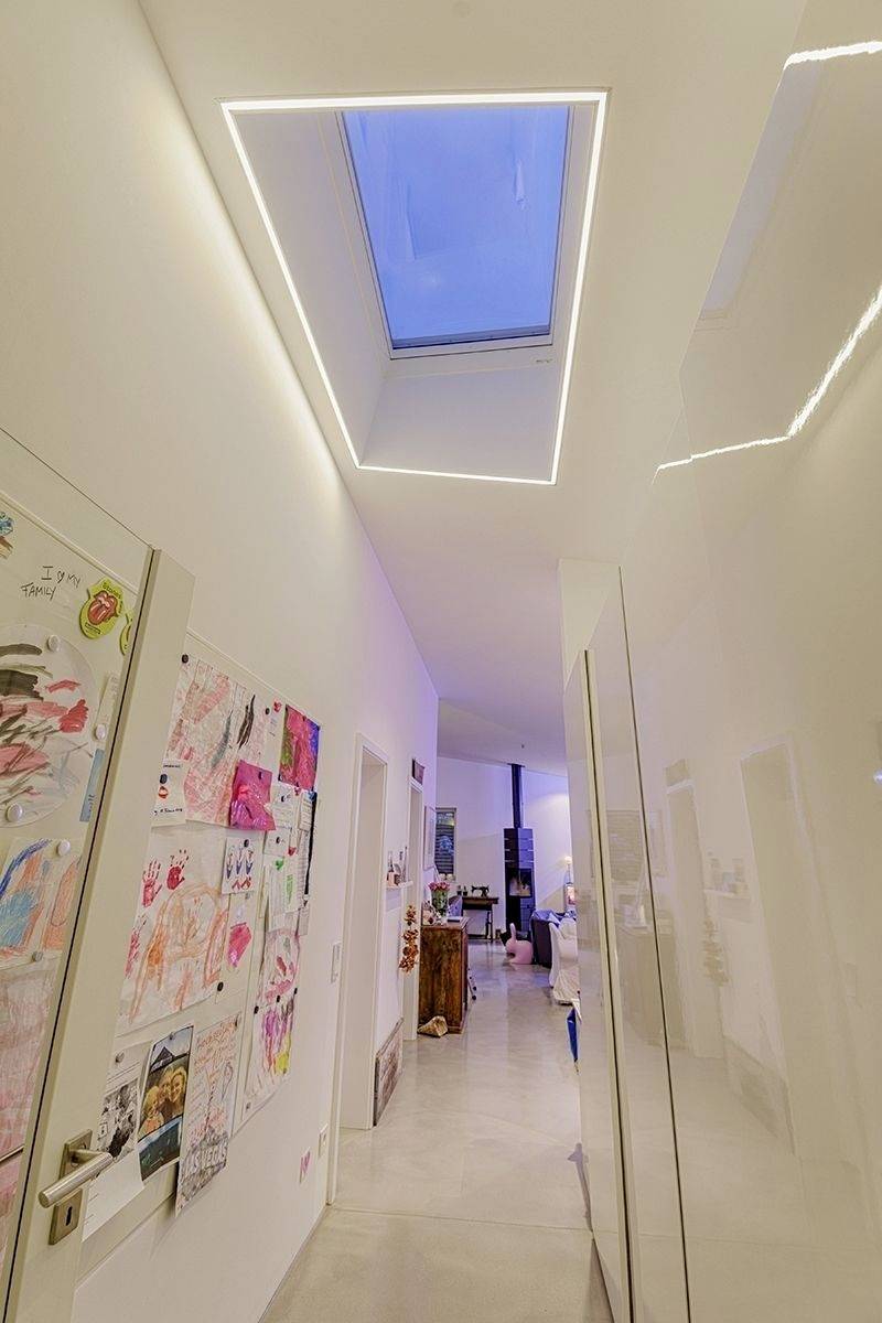 Flur mit hellem Fußboden und Decke. Links bunte Kinderzeichnungen an der Wand. Oberlichter lassen Tageslicht herein. Gemütliche Atmosphäre.