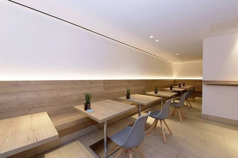 Minimalistisches Café-Interieur mit Holzverkleidung, modernen Tischen und grauen Stühlen, warm beleuchtete, einladende Atmosphäre.