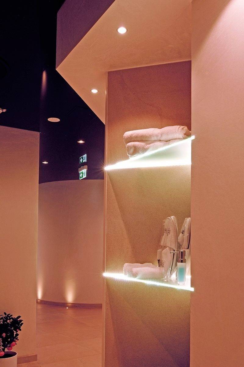Ein Spa-Wartebereich mit sanfter Beleuchtung, zwei beleuchtete Regale mit Handtüchern und Pflegeprodukten, entspannte Atmosphäre.