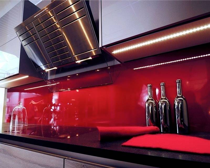 Moderne Küche mit rotem Hochglanz-Backsplash, schwarzer Arbeitsfläche und drei glänzenden Flaschen als Dekoration.