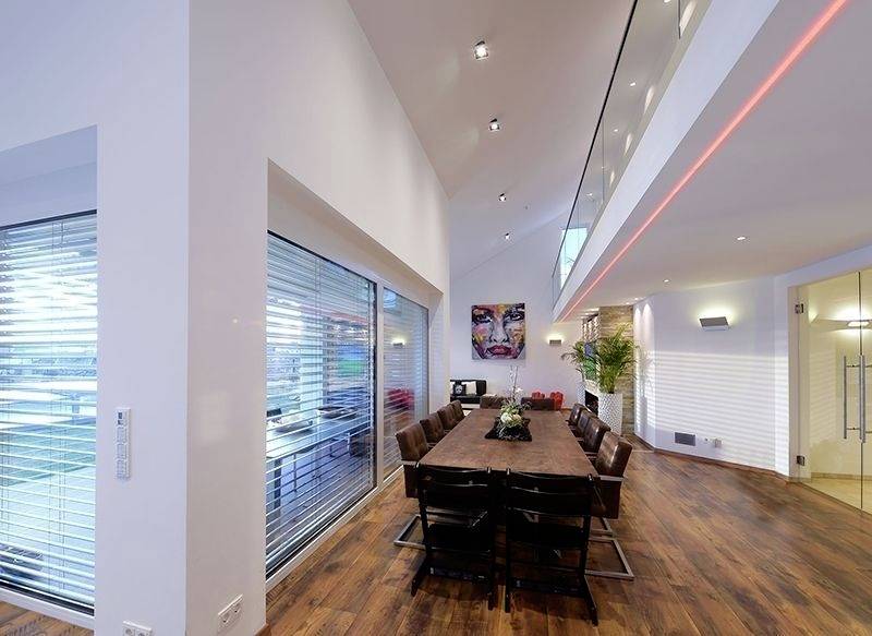 Esszimmer mit langem Holztisch, Lederstühlen und hoher Decke. Große Fenster lassen viel Licht herein. Moderne Kunst an der Wand.