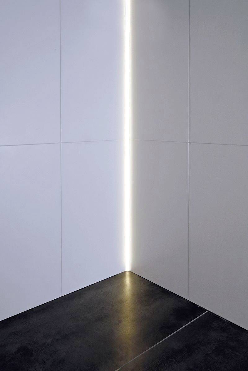 Raum mit dunklem Boden und weißen Wänden; eine vertikale Lichtlinie in der Ecke erzeugt einen modernen, minimalistischen Look.