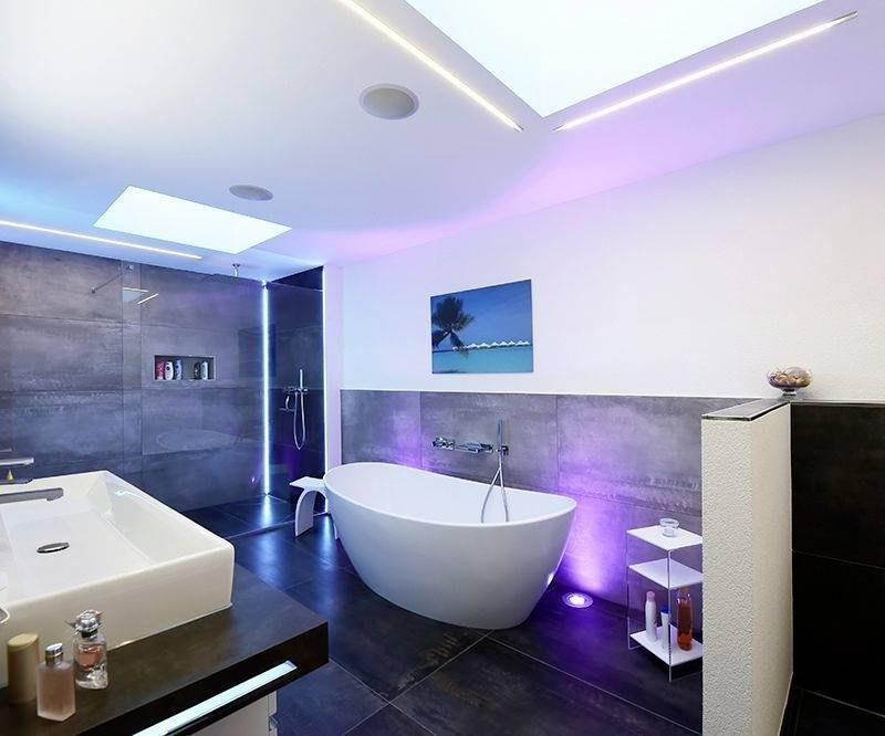 Modernes Badezimmer mit freistehender Badewanne, großem Waschbecken und Regendusche. LED-Beleuchtung in Blau und Purpur.