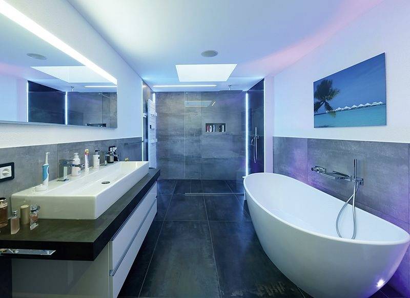 Modernes Badezimmer mit freistehender Badewanne, großem Waschbecken und beleuchtetem Spiegel. Schlichte, elegante Gestaltung.