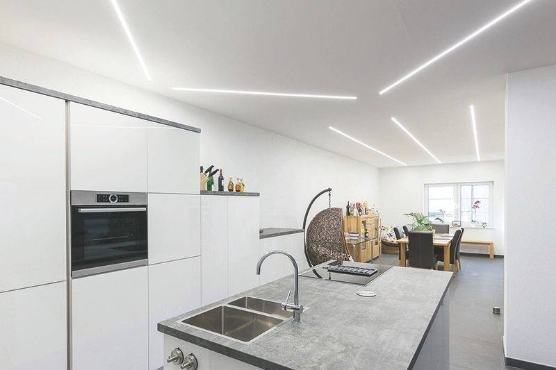 Moderne Küche mit grauer Arbeitsplatte, eingebautem Ofen und Spüle. Im Hintergrund helle Essbereich mit Fenster und Pflanzen.