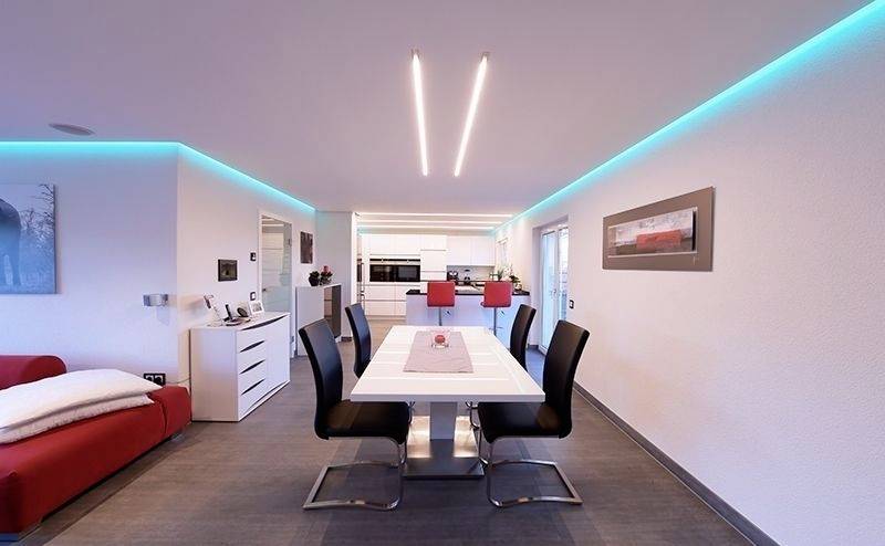 Moderne Küche mit Essbereich. Weiße Wände, schwarzer Tisch mit sechs Stühlen, rote Akzente in der Küche. Blaues LED-Licht an Decke.