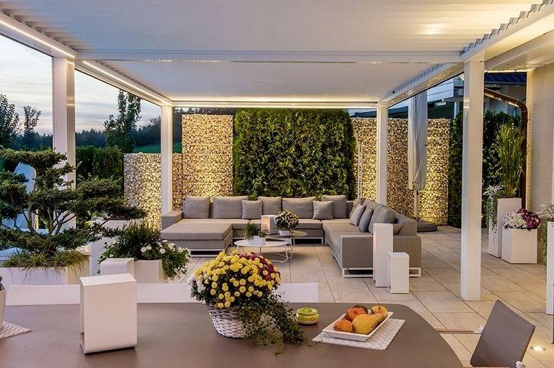 Moderner Terrassenbereich mit großen Sofas, dekorativen Pflanzen, Korbmöbeln und stimmungsvoller Beleuchtung bei Sonnenuntergang.