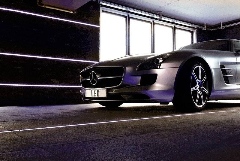 Ein silbernes Auto steht in einer Garage mit Neonbeleuchtung. Am vorderen Kennzeichen steht 'LEO'.