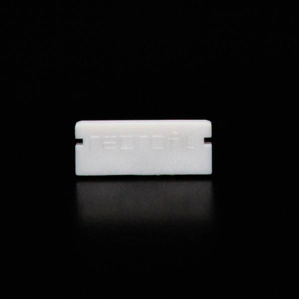 Eine weiße Rasierklinge mit glatter Oberfläche liegt vor schwarzem Hintergrund.