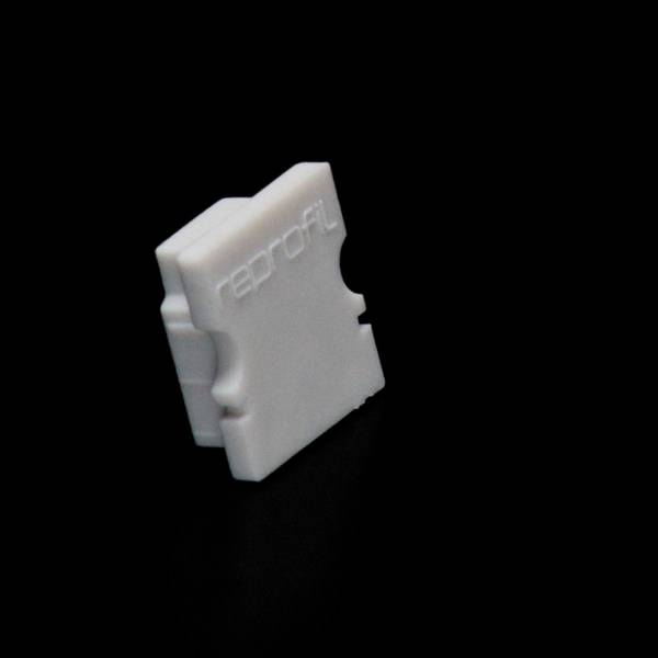 Ein weißer, kunststoffartiger Kabelclips mit der Aufschrift 'reprofil' auf dunklem Hintergrund.