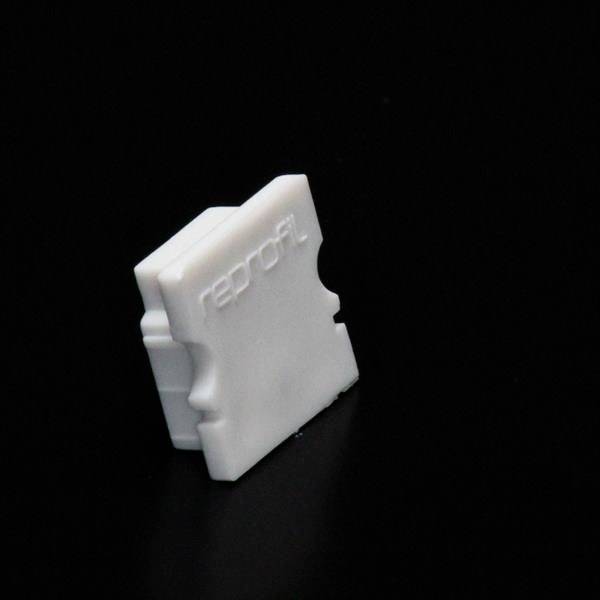 Ein weißes, gleichmäßig geformtes Kunststoffteil mit der Prägung 'reprap' sichtbar auf schwarzem Hintergrund.