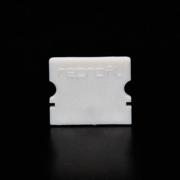 Ein weißes Plastikobjekt in Form einer Rasierklinge auf schwarzem Hintergrund. Es hat eine zentrale Aussparung und den eingeprägten Schriftzug 'neprot'.