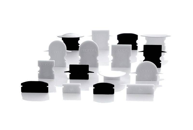 Verschiedene schwarze und weiße Kunststoffteile mit geschwungenen und geraden Oberflächen, reflektieren auf glänzendem Untergrund.