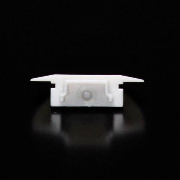 Ein weißes Kunststoffteil auf schwarzem Hintergrund. Es scheint aus zwei flachen, leicht abstehenden Teilen und einer zentralen Halterung zu bestehen.