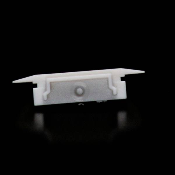 Ein weißes, rechteckiges Kunststoffteil mit Haken auf schwarzem Hintergrund. Es sieht aus wie ein Montage- oder Verbindungselement.