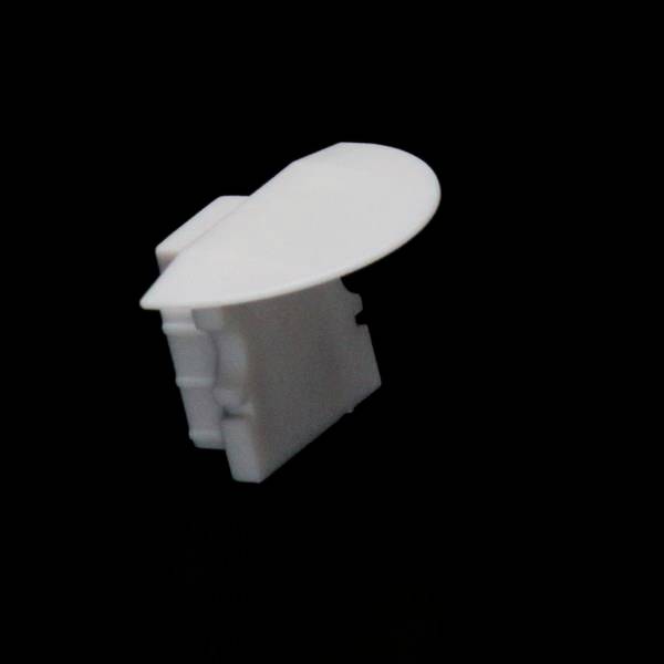 Ein weißes Kunststoffobjekt mit einer ovalen, flachen Oberseite und rechteckiger Basis vor schwarzem Hintergrund.