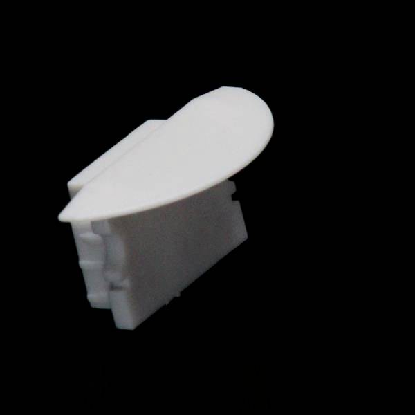 Weißes, abgerundetes Kunststoffteil, möglicherweise ein Gehäuse- oder Verbindungselement, vor schwarzem Hintergrund.