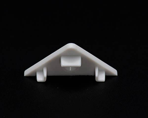 Ein weißes, dreieckiges Kunststoffobjekt mit vier Halterungen auf einer schwarzen Oberfläche platziert.