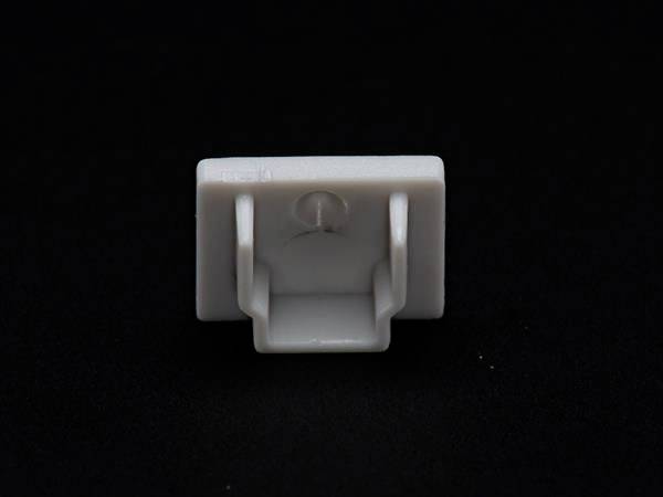 Ein weißer Kunststoffhaken auf schwarzem Hintergrund. Der Haken ist quadratisch mit zwei seitlichen Halterungen.