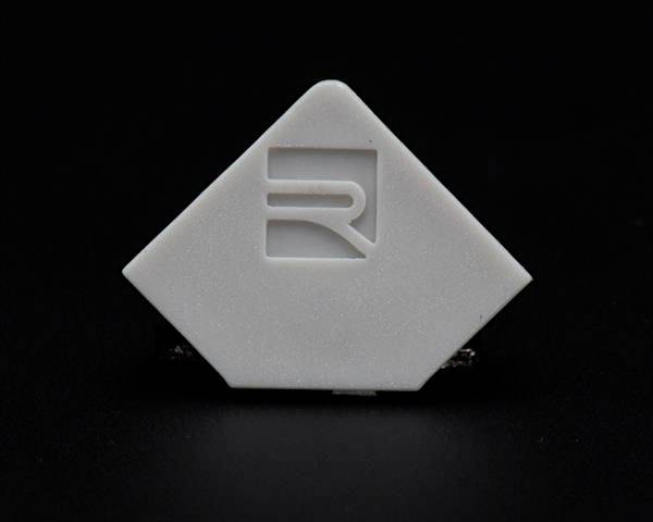 Weißes, rautenförmiges Objekt mit einem eingravierten stilisierten Symbol auf dunklem Hintergrund.