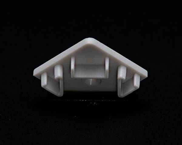 Ein weißes, dreieckiges Kunststoffobjekt mit drei Haken, auf schwarzem Hintergrund.