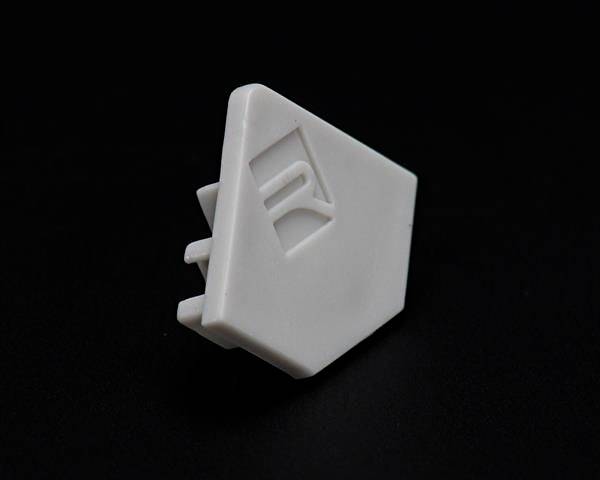Ein weißes, dreieckiges Kunststoffteil mit drei abstehenden Stiften und einer erhabenen Zahl '1', auf schwarzem Hintergrund.