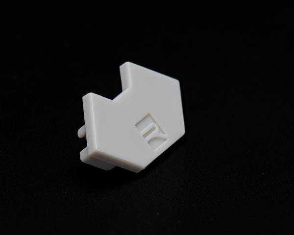 Ein kleines weißes, rechteckiges Kunststoffstück mit einer eingravierten Linie. Es liegt auf einem dunklen Hintergrund.
