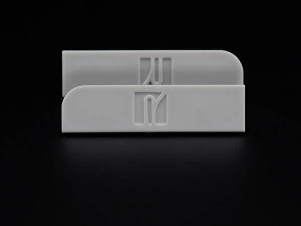 Zwei hellgraue, rechteckige Kunststoffe mit abgerundeten Ecken auf schwarzem Hintergrund, beide mit einem stilisierten Logo oder Symbol.