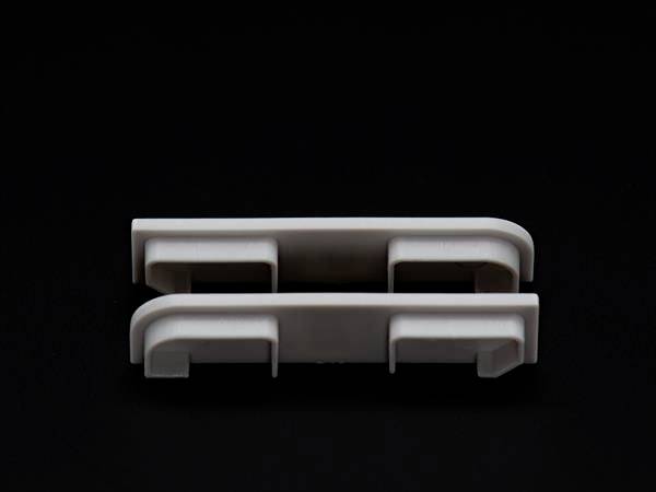 Zwei weiße, längliche Kunststoffclips auf schwarzem Hintergrund, übereinander liegend.