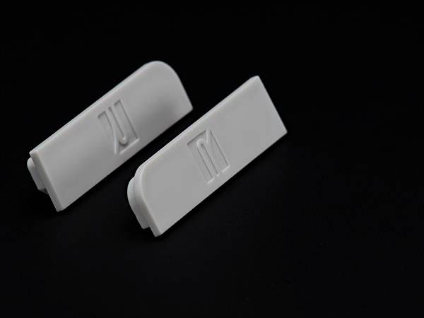 Zwei weiße Kunststoffclips liegen auf schwarzem Hintergrund, einer mit einer gebogenen Kante, der andere mit einer geraden Kante.