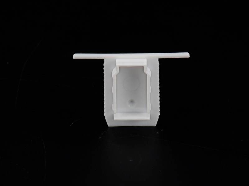 Weiße Kunststoffkomponente mit rechteckiger Öffnung in der Mitte, auf schwarzem Hintergrund. Könnte Teil eines größeren technischen Geräts sein.