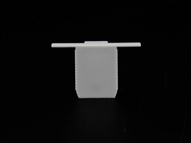 Ein weißer Kunststoffclip in Form eines T auf schwarzem Hintergrund.