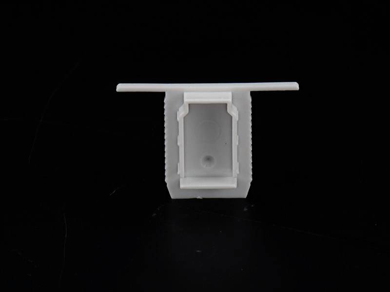 Ein quadratischer, weißer Kunststoffverschluss auf schwarzem Hintergrund, möglicherweise ein Deckel oder Adapterelement.