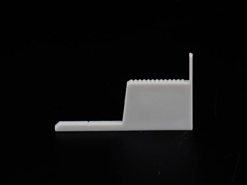 Eine weiße, rechteckige Kunststoffhalterung mit gezahntem Ende und kleinem Vorsprung auf schwarzem Hintergrund.