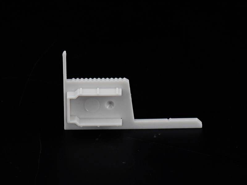 Ein weißer Kunststoffwinkel auf schwarzem Hintergrund, vermutlich ein Bauteil oder Befestigungselement, zeigt Kanten und strukturelle Details.